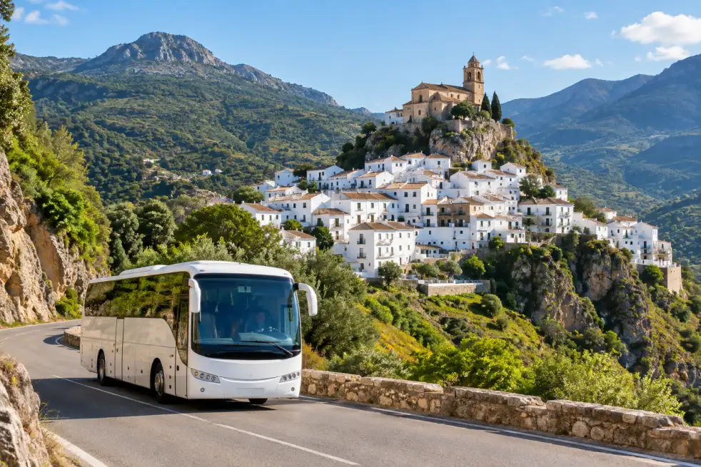 Autocar en una carretera de montaña junto a un pueblo blanco de la Sierra de Cádiz